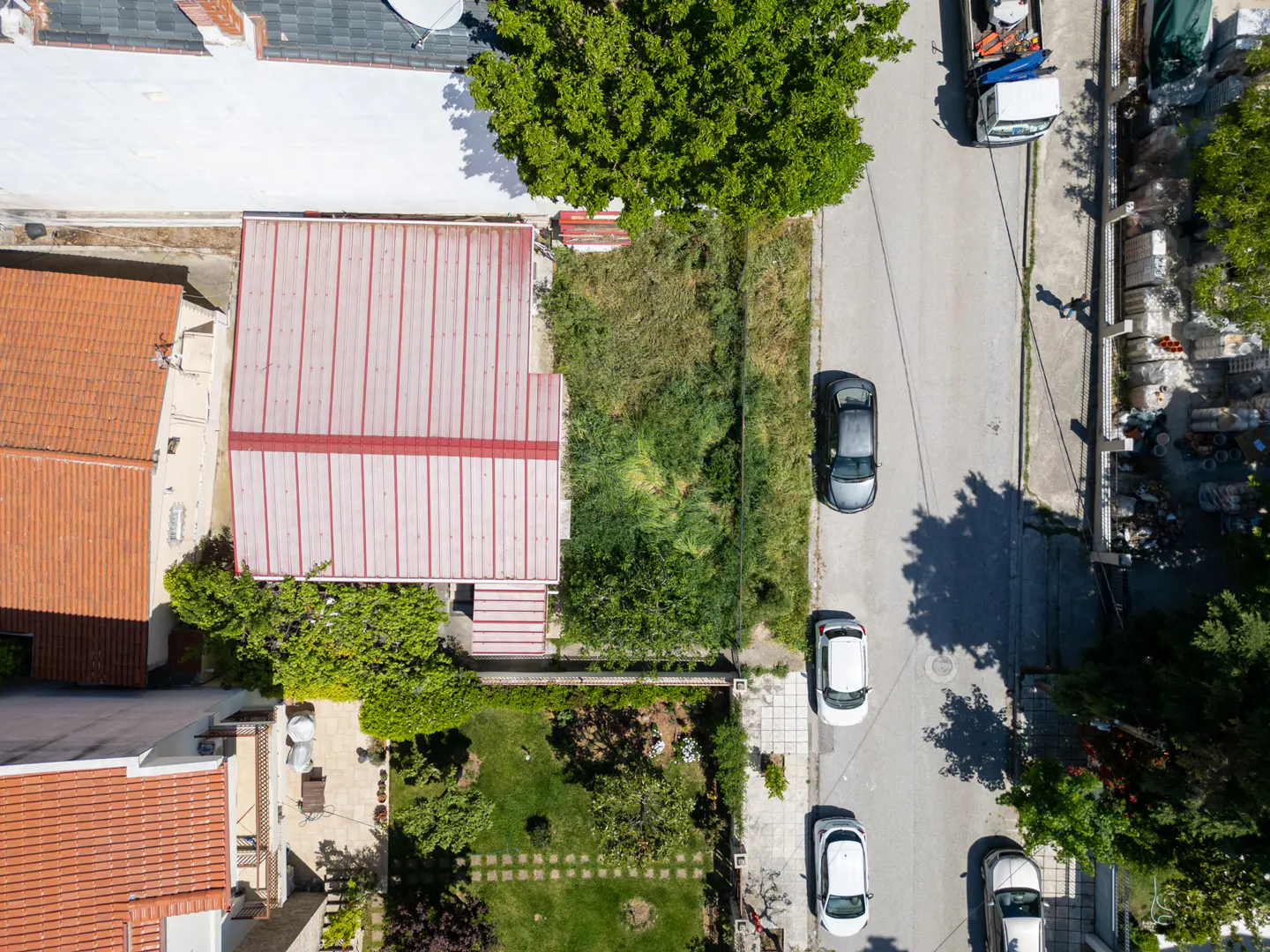 Aerial view of a property with a red-roofed building, green lawn, and a street with parked cars.