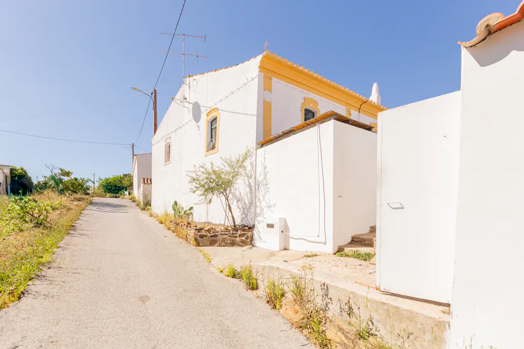 Exterior view of a white building with yellow trim along a narrow street under a clear blue sky.