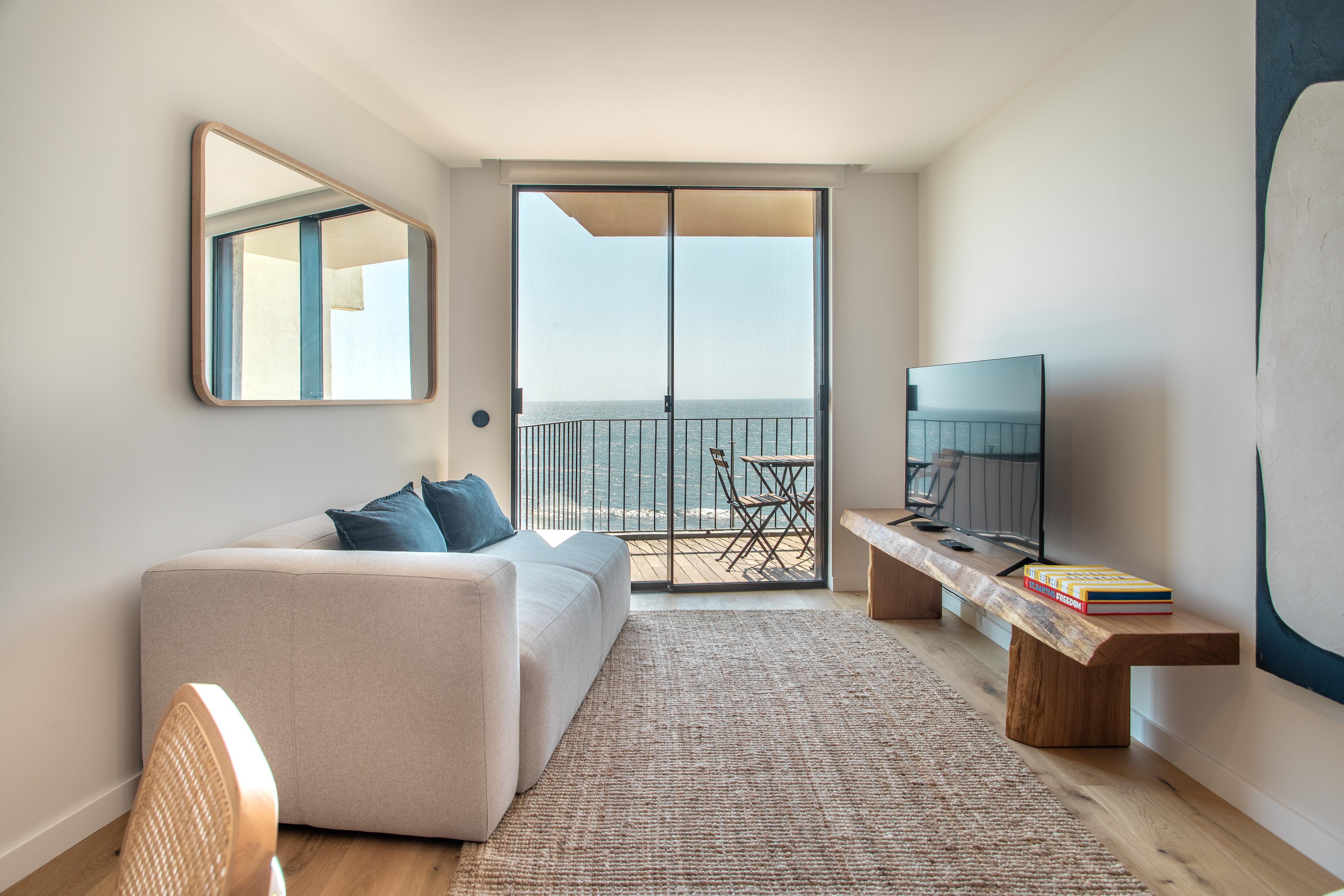Modern living room with a white sofa, live-edge wood media console, and a balcony overlooking the ocean. [AI-generated text]