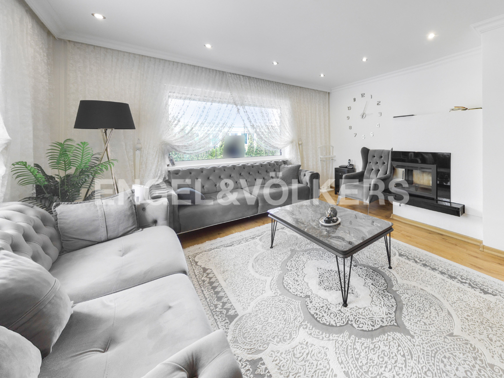 Modern living room with grey tufted sofas, a marble coffee table, a fireplace, and a large wall clock on white walls.