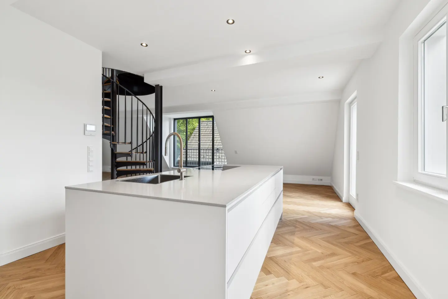 Bright, modern kitchen with white cabinets, countertops, and walls. A black spiral staircase is visible. Wood floors and natural light.