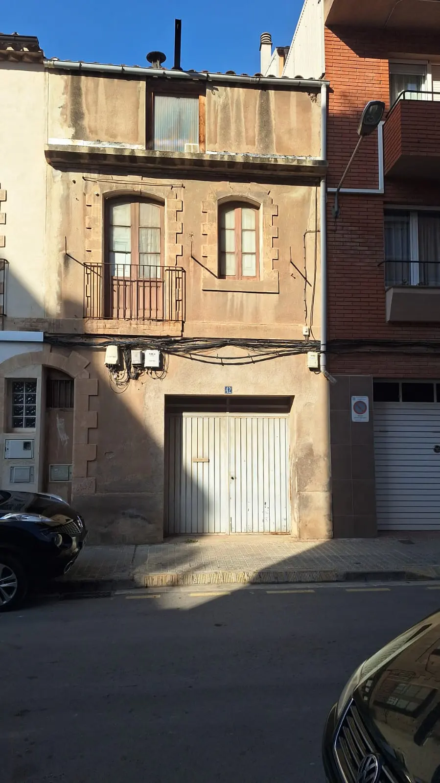 Two-story beige building with a garage door on the ground floor and a small balcony on the second floor.