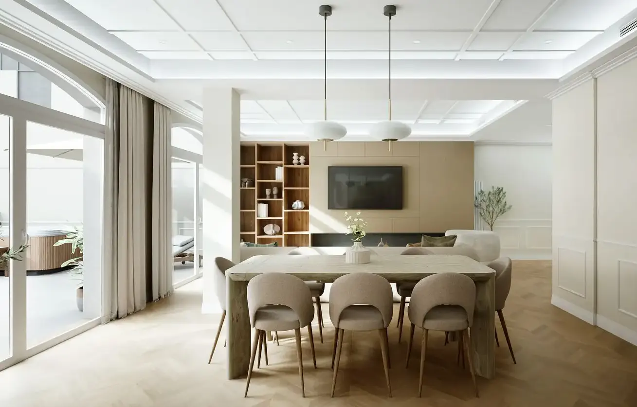 Bright, modern dining room with a long wooden table, beige chairs, and pendant lights. A bookshelf and TV are in the background.