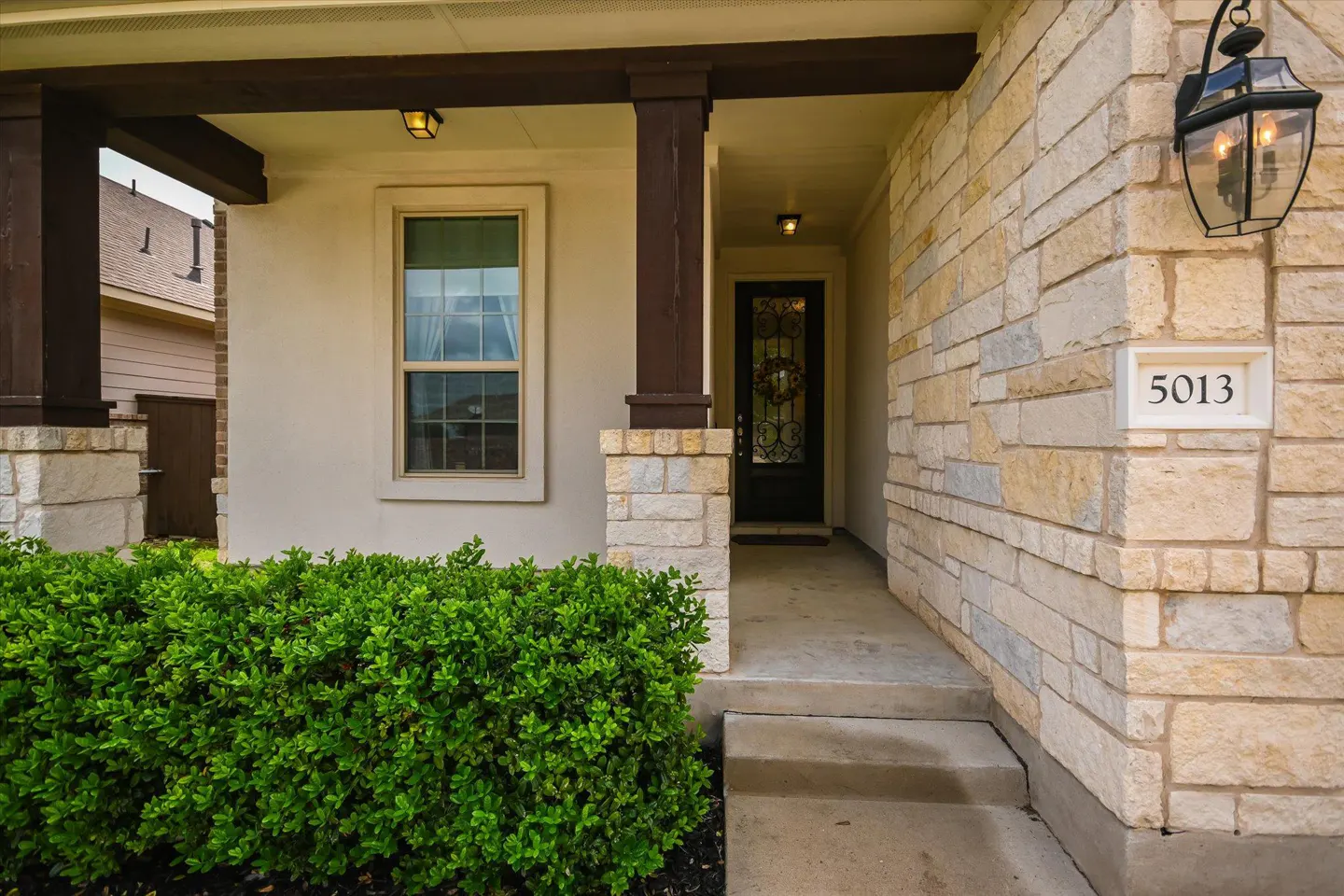 Front entrance of a house with stone facade, dark brown pillars, green bush, and the number 5013.