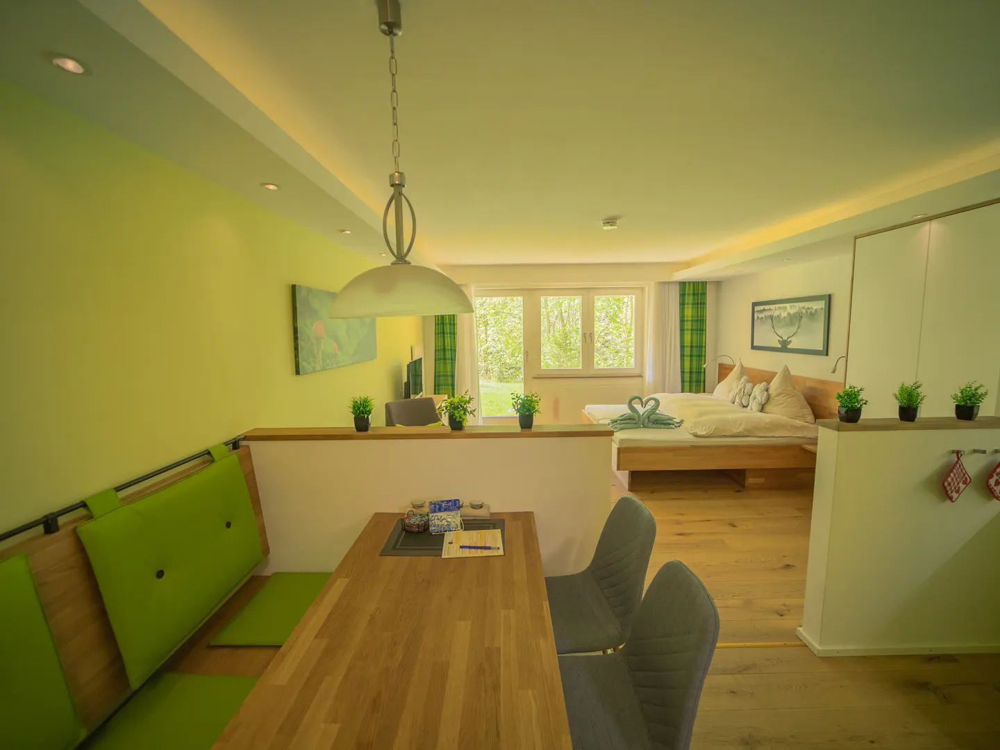 Studio apartment with green walls, a dining area with a green bench, and a bed with swan-shaped towels.