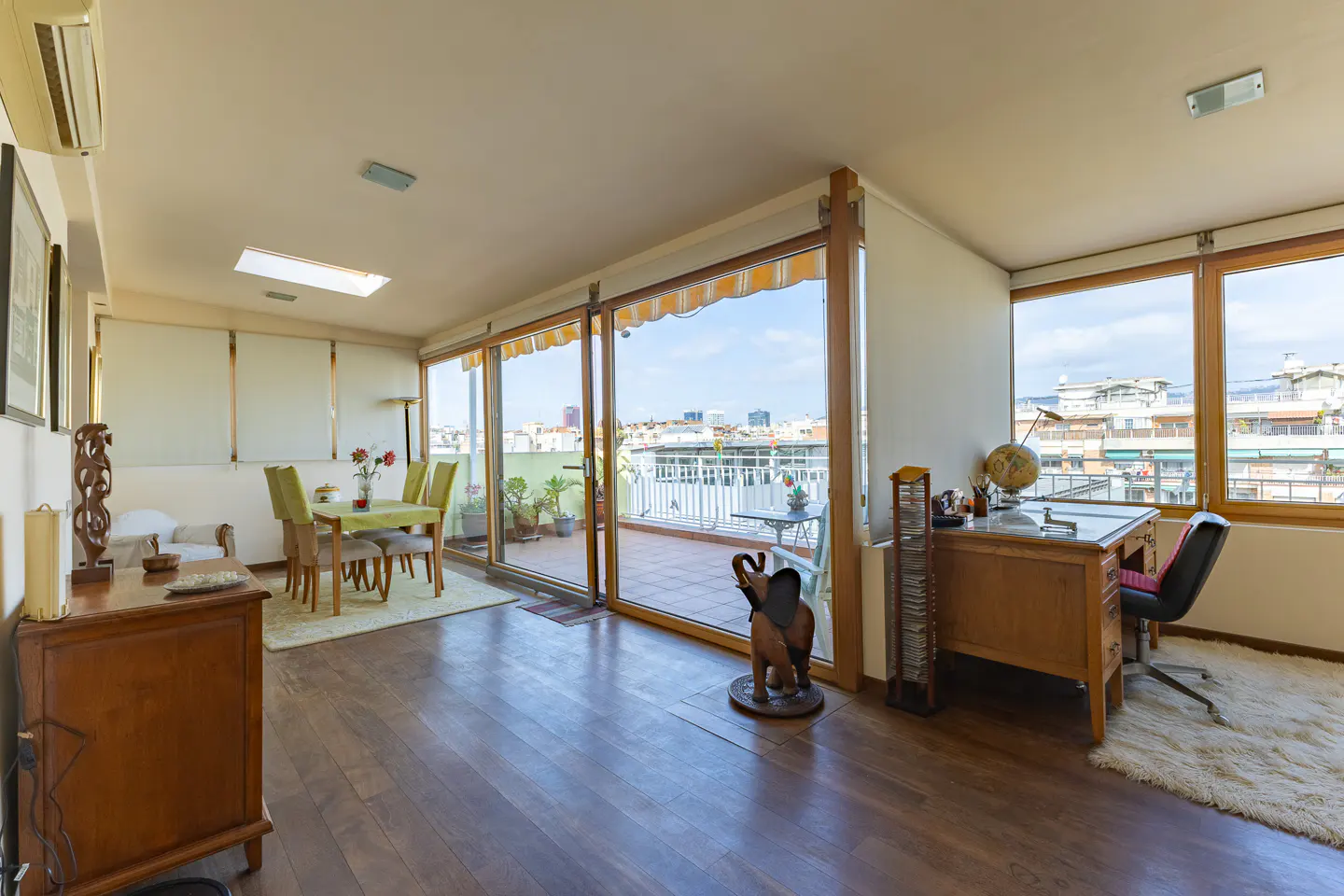 Bright living room with wood floors, dining table, desk, and balcony with city views.