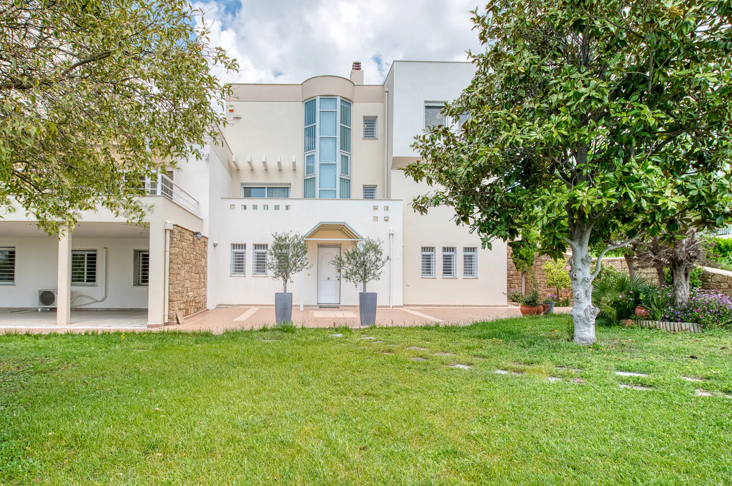 A modern, two-story white house with a green lawn and trees in the front yard.