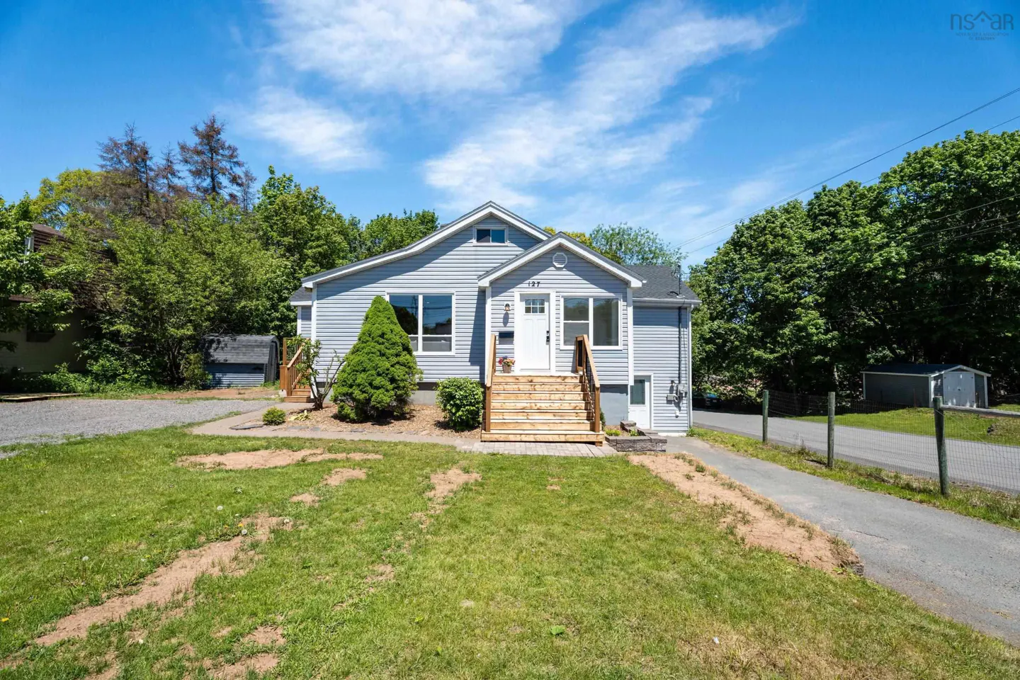 Light blue bungalow with white trim, wooden front steps, and a green lawn under a bright blue sky.