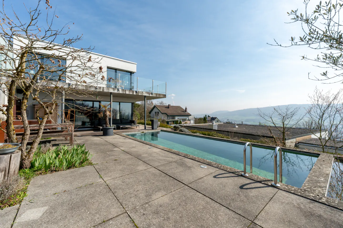 Modern white house with a long rectangular swimming pool on a concrete patio overlooking a scenic valley landscape.