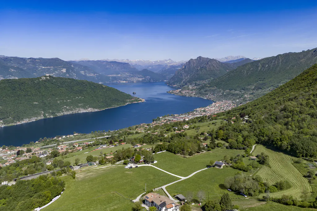 Aerial view of a blue lake surrounded by green mountains and a small town under a clear blue sky.