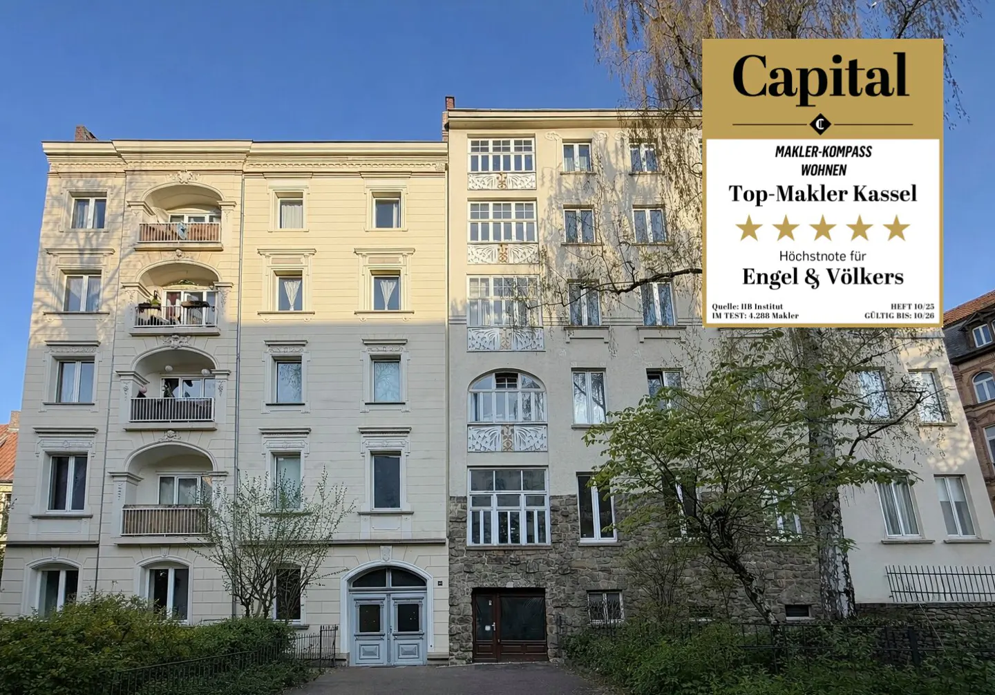 Exterior of a light beige apartment building with balconies and a "Top-Makler Kassel" award.