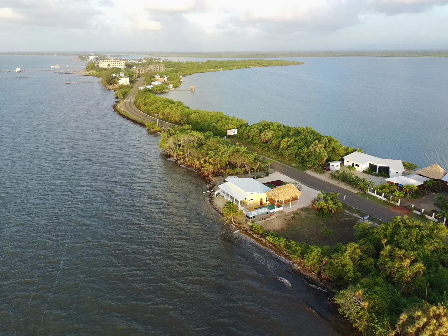 Aerial view of a narrow strip of land with a road, buildings, and lush green vegetation, bordered by blue water on both sides.