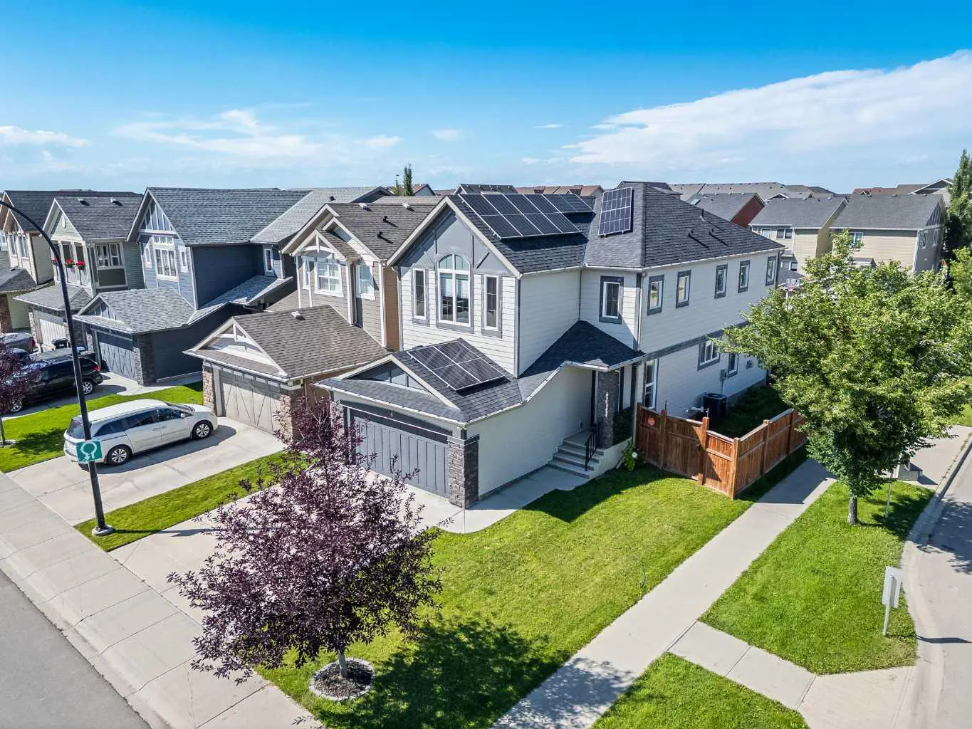 Aerial view of a two-story house with solar panels on the roof in a suburban neighborhood on a sunny day.