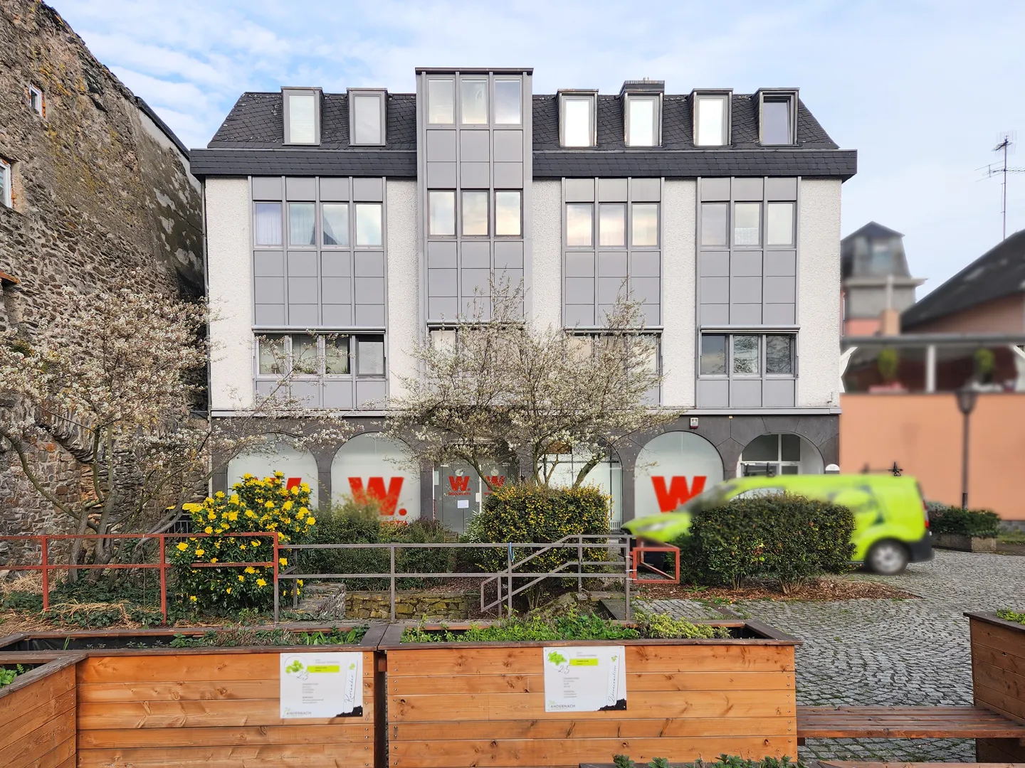 Three-story white building with gray trim and a black roof, with red "W" logos on the ground floor.