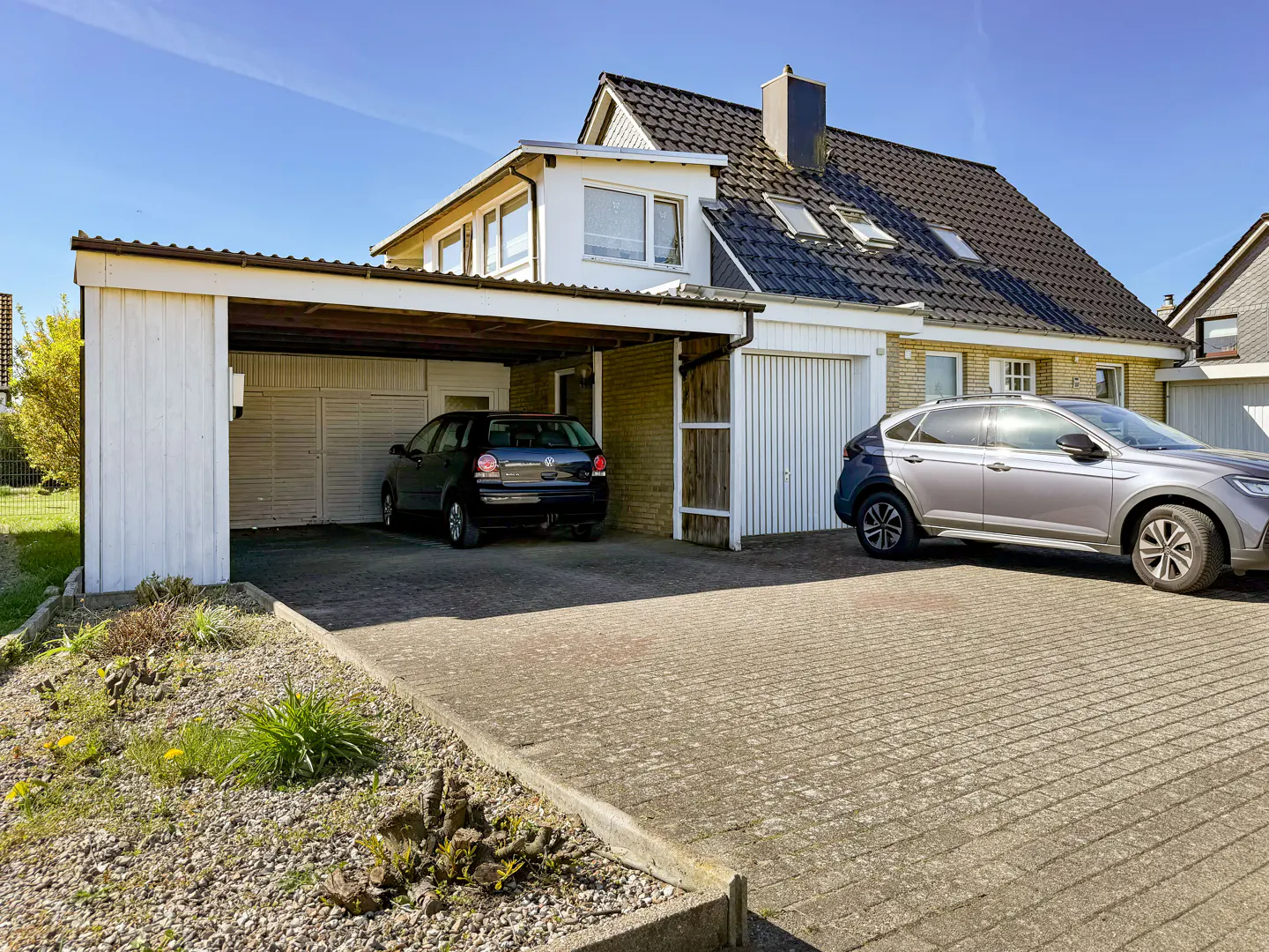 Exterior of a two-story house with a black car in the carport and a silver car parked in the driveway.