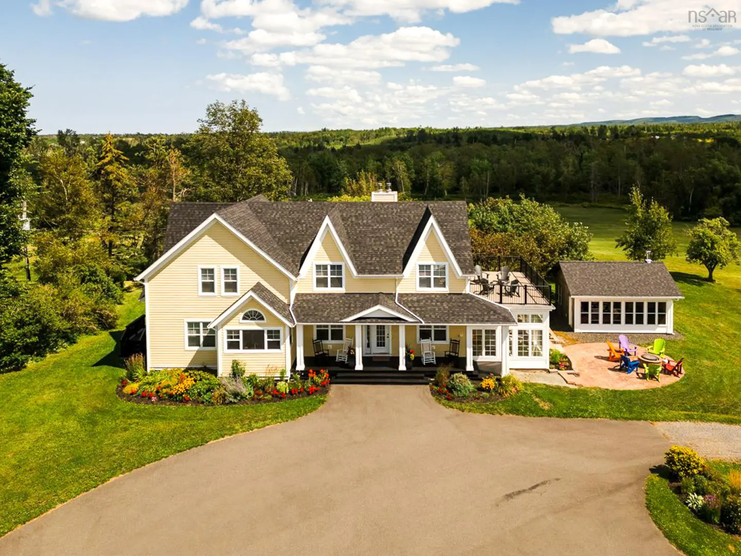 Aerial view of a yellow two-story house with a gray roof, white trim, and a long driveway on a sunny day.