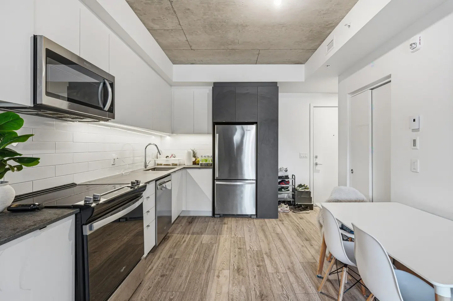 A modern kitchen with white cabinets, stainless steel appliances, and a dining area with a white table and chairs.