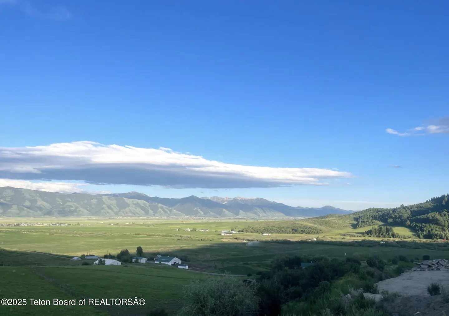 Scenic view of green fields and mountains under a blue sky with white clouds. Small white houses dot the landscape.