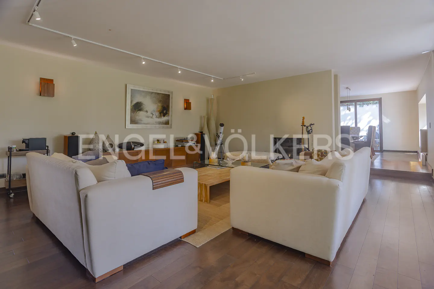 Living room with two white sofas, a wooden coffee table, and dark wood floors. Artwork hangs on the beige walls.