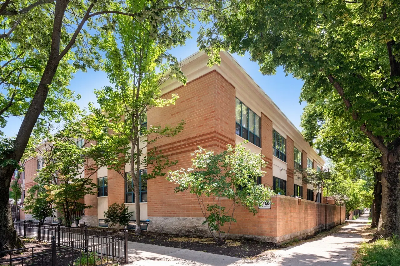 Exterior view of a two-story brick building with large windows and a white trim, surrounded by green trees.