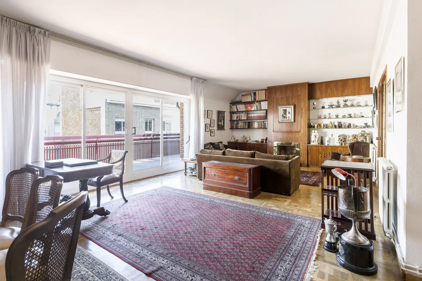 A living room with a red patterned rug, brown sofa, wood paneling, and a balcony with sliding glass doors.