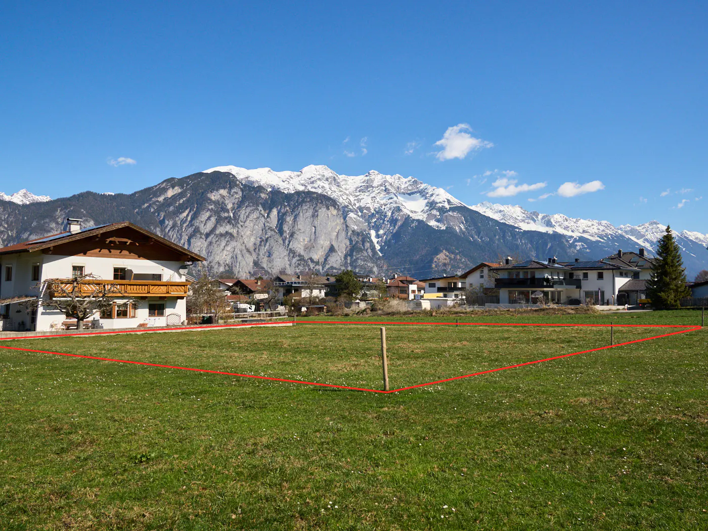 Vacant lot with a red boundary line, green grass, and mountain views under a blue sky.