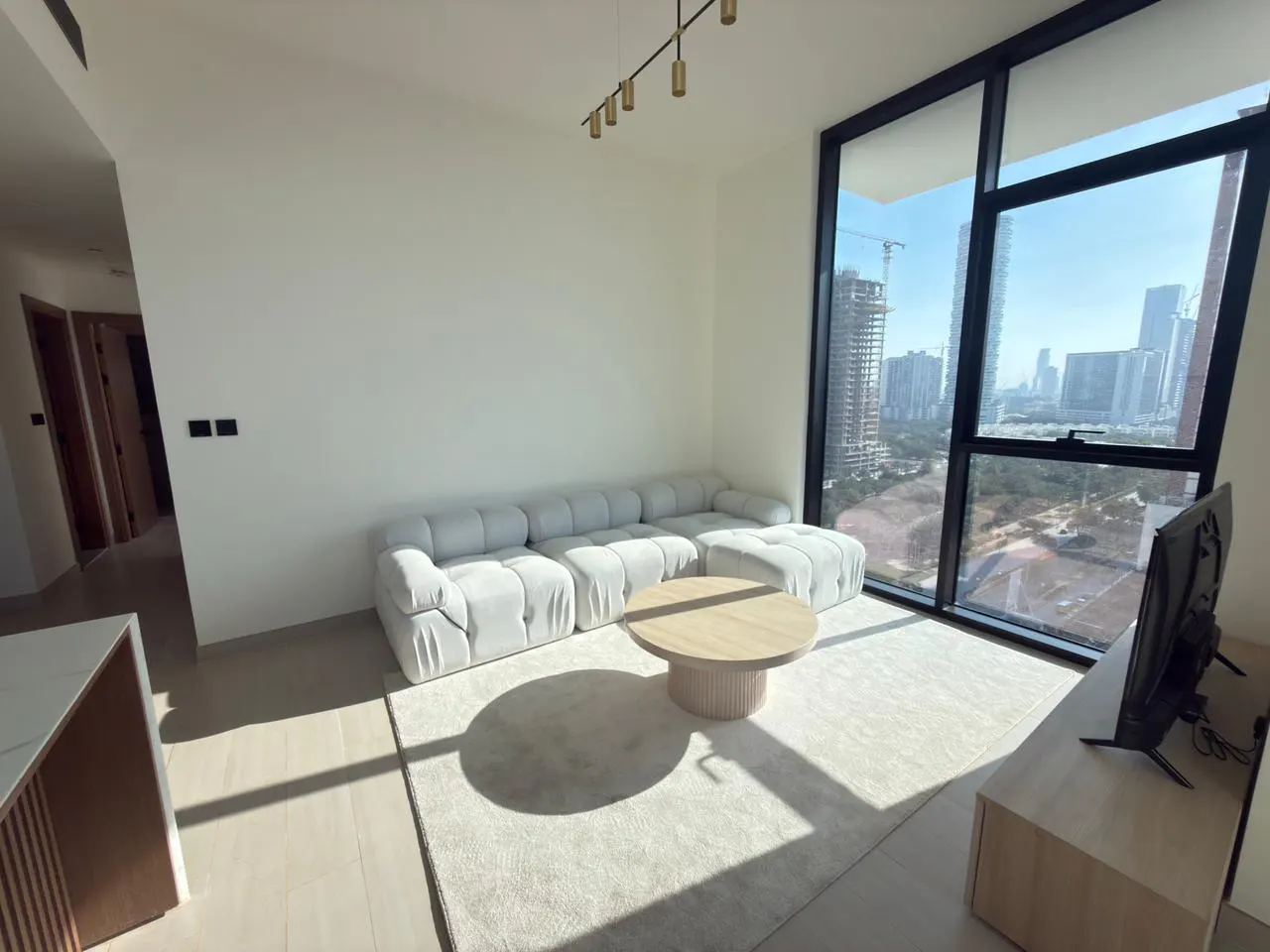 Bright living room with a white sectional sofa, round wood table, and large windows with a city view.