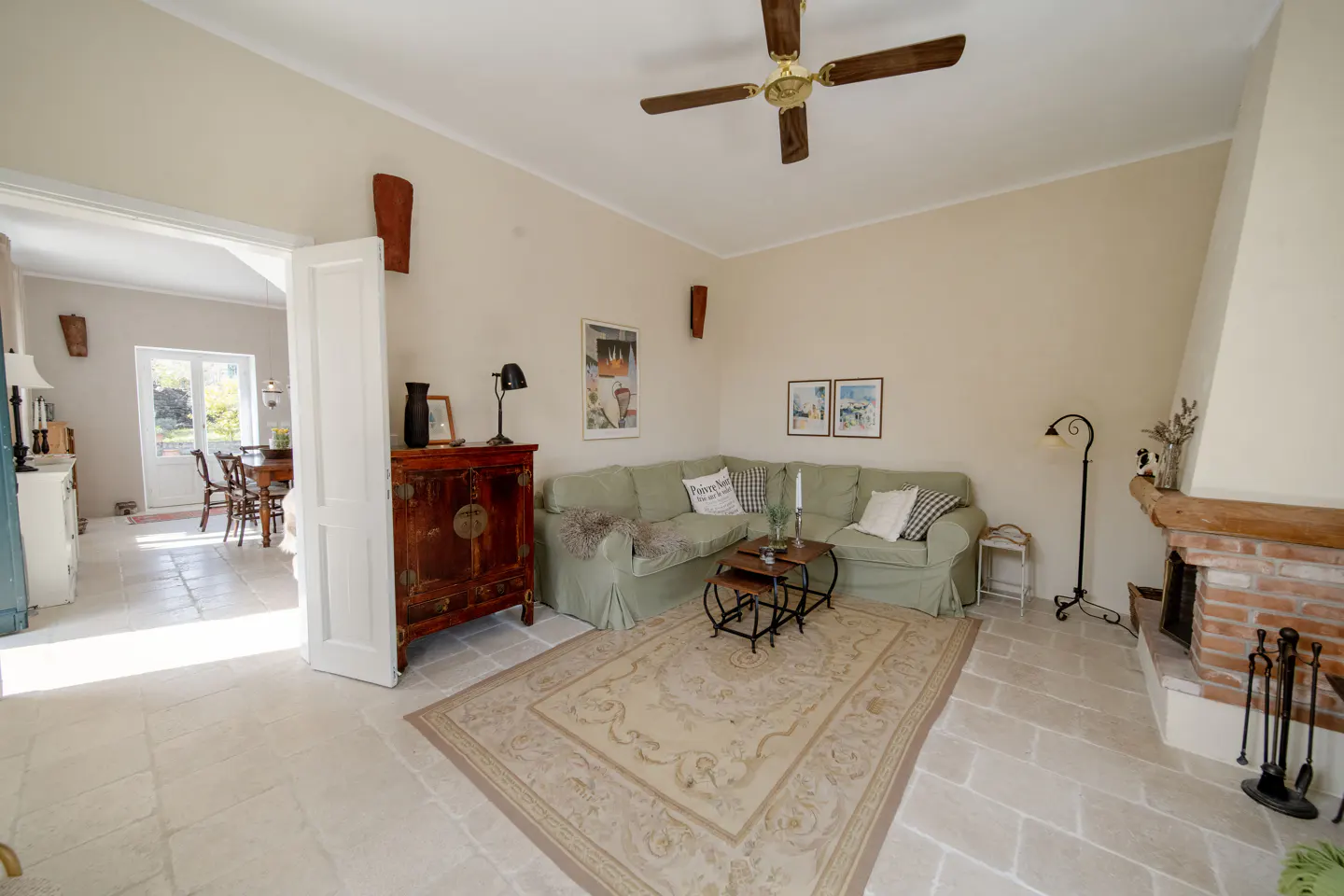 Living room with light green sofa, patterned rug, and brick fireplace. A dining room is visible through an open doorway.