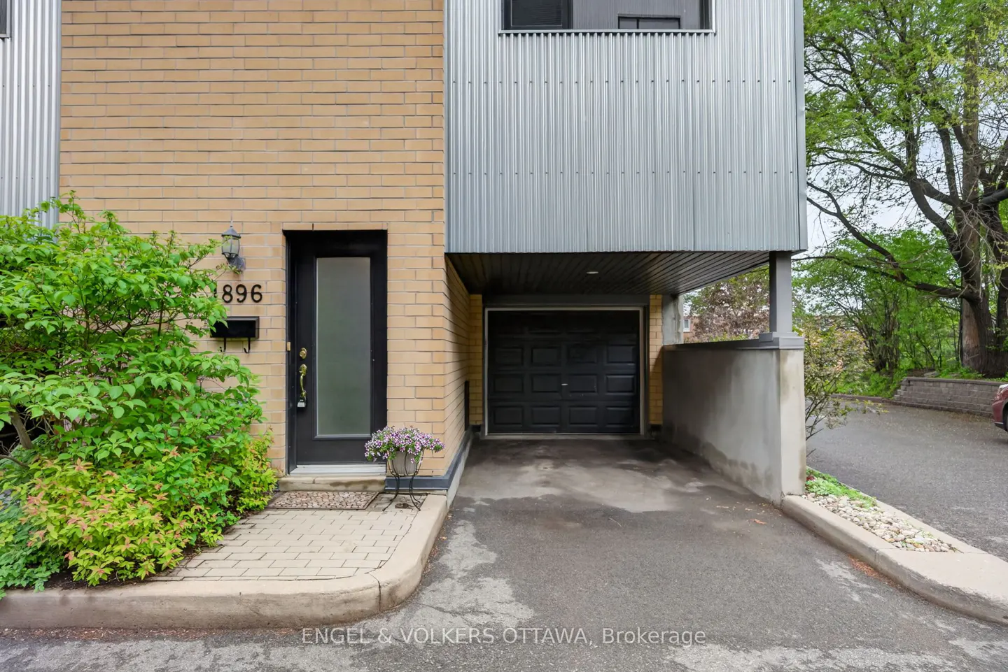 Exterior of a two-story townhouse with a black door, garage, and brick and metal siding.
