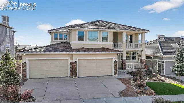 Two-story beige house with a brown roof, two-car garage, and a balcony on a sunny day.