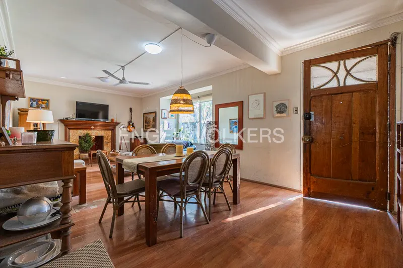 A living and dining area with hardwood floors, a wooden dining table with six chairs, and a fireplace with a TV above it.