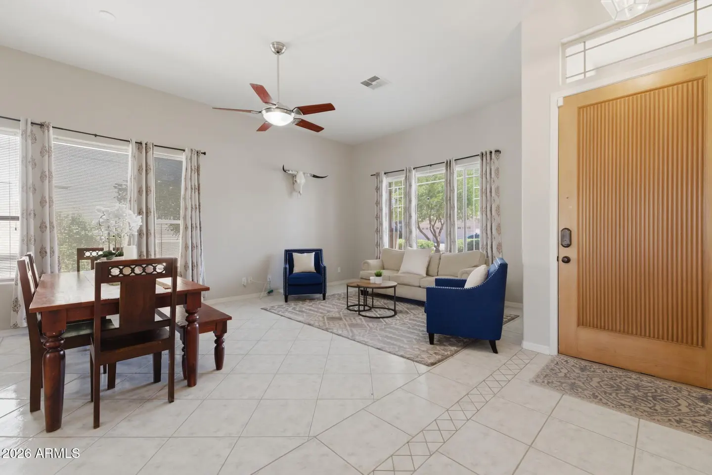 Open-concept living and dining area with tile floors, a wooden dining set, blue armchairs, and a beige sofa.