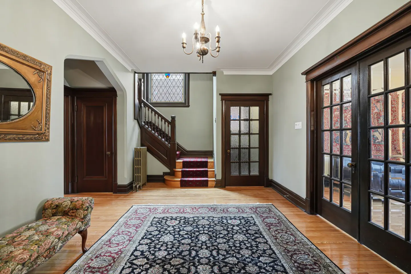 Entryway with hardwood floors, a floral rug, and a staircase with a red runner. A chandelier hangs from the ceiling.