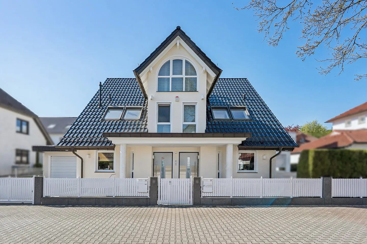 A two-story house with a black roof and white fence on a sunny day.