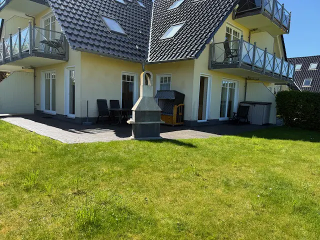 Two-story yellow house with balconies, a patio with furniture, a grill, and a green lawn.