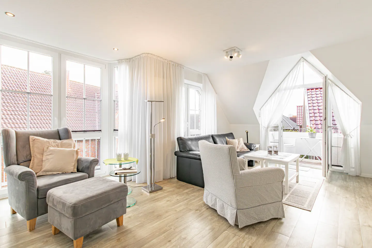 Bright living room with gray armchair, black sofa, and white balcony doors draped with sheer curtains.