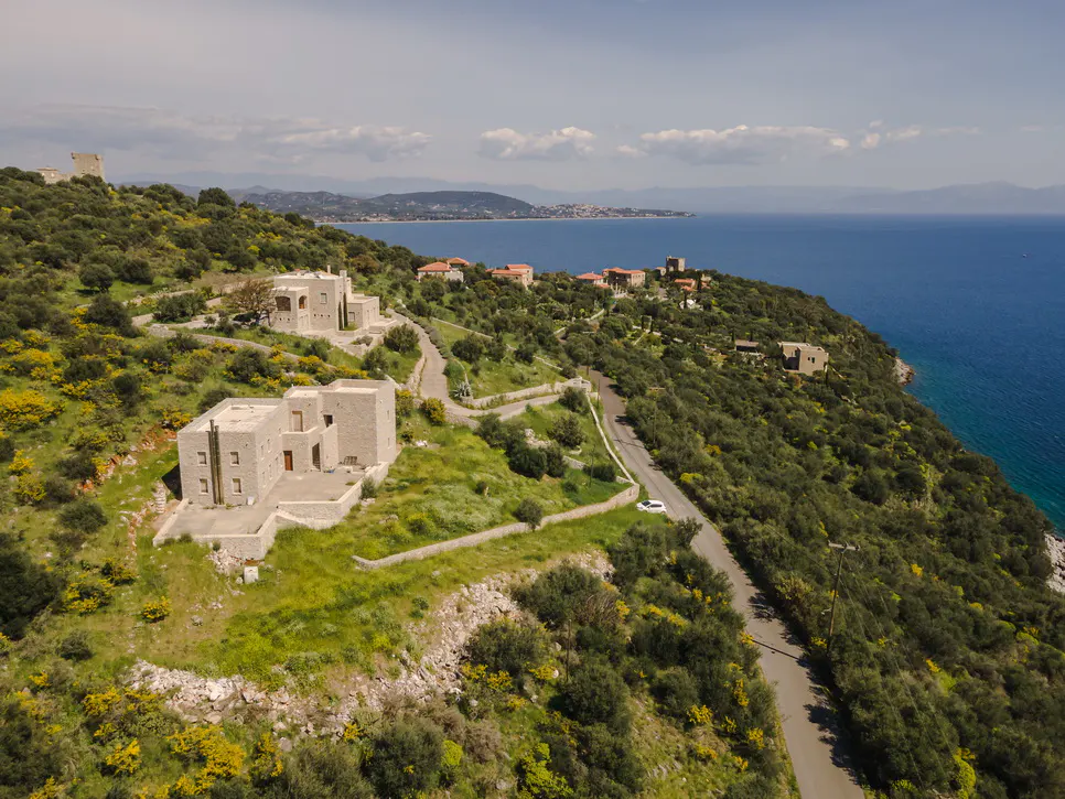 Aerial view of stone houses on a green hillside overlooking the blue sea and distant coastline.