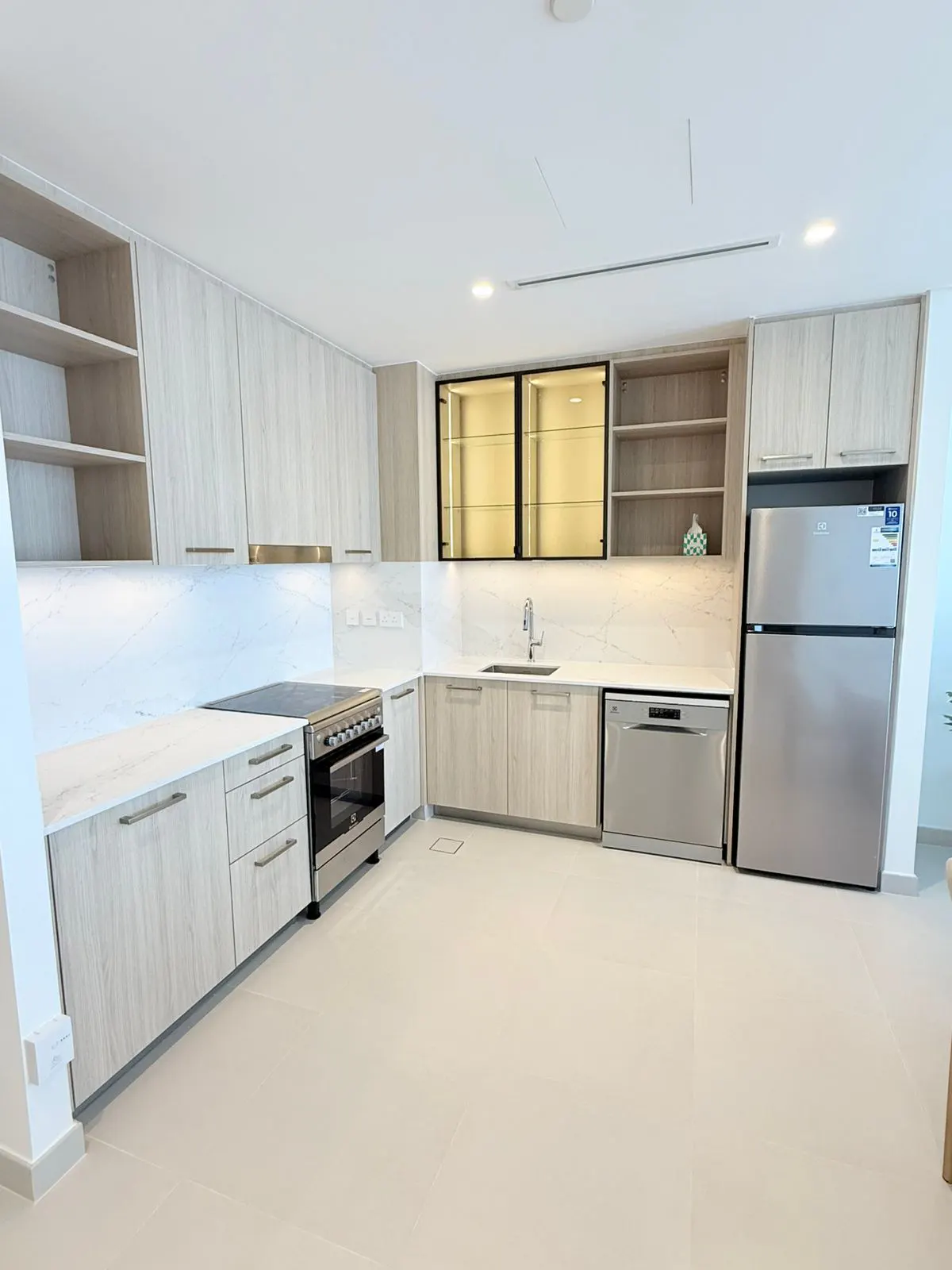 Modern kitchen with light wood cabinets, white marble backsplash, stainless steel appliances, and a large refrigerator.