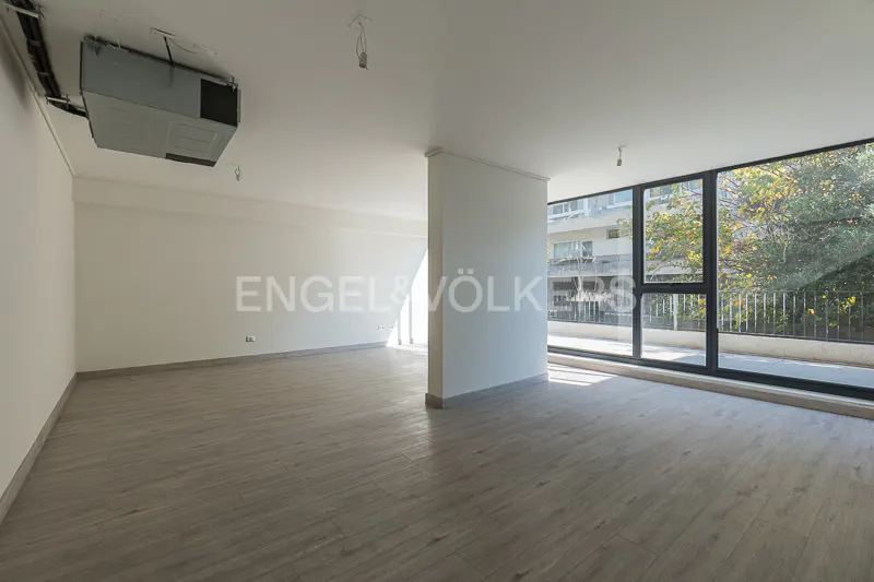 Bright, empty room with light wood floors, white walls, and large windows showing trees and a building. An AC unit is visible on the ceiling.