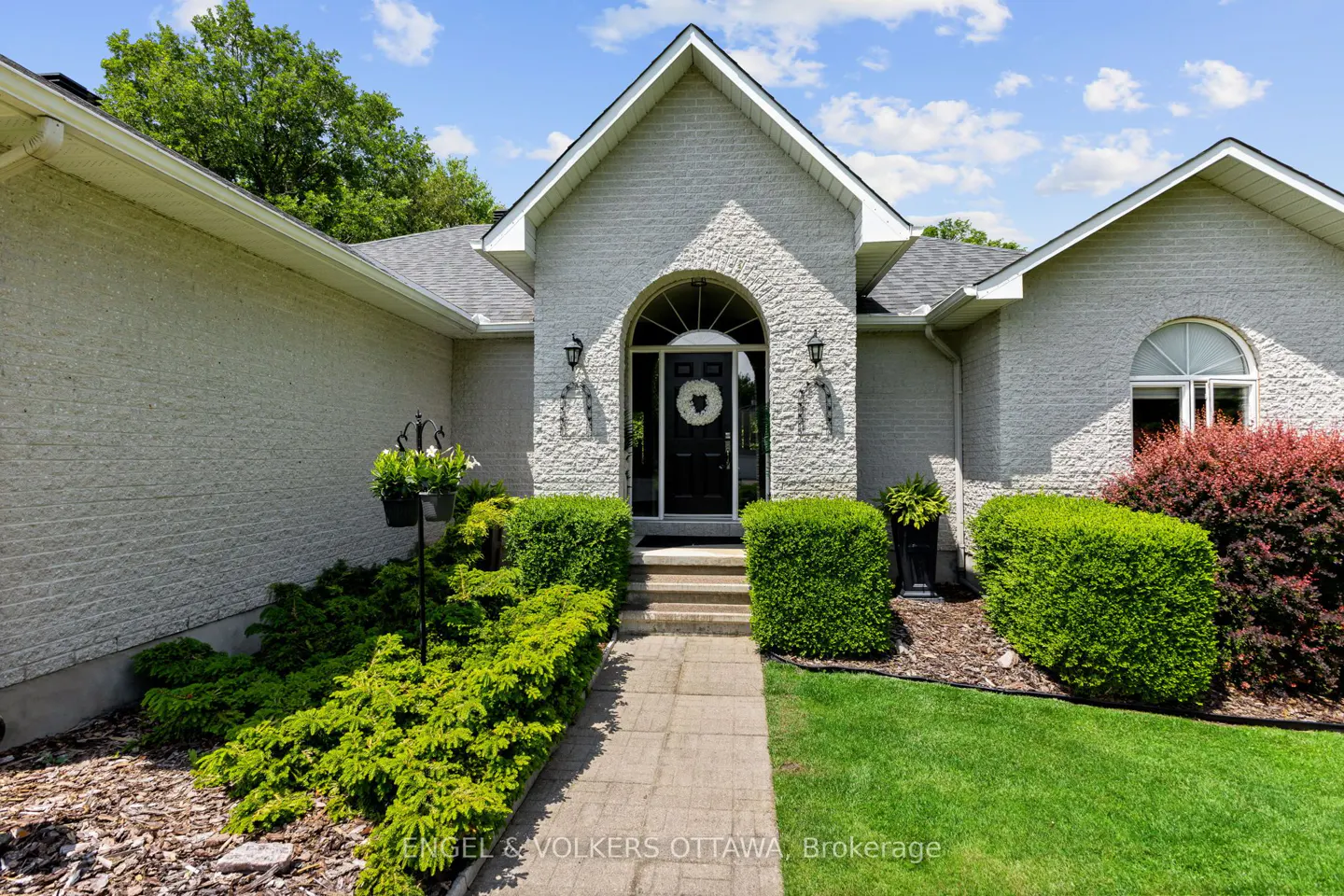 Exterior of a light gray brick house with a black front door and manicured green landscaping.