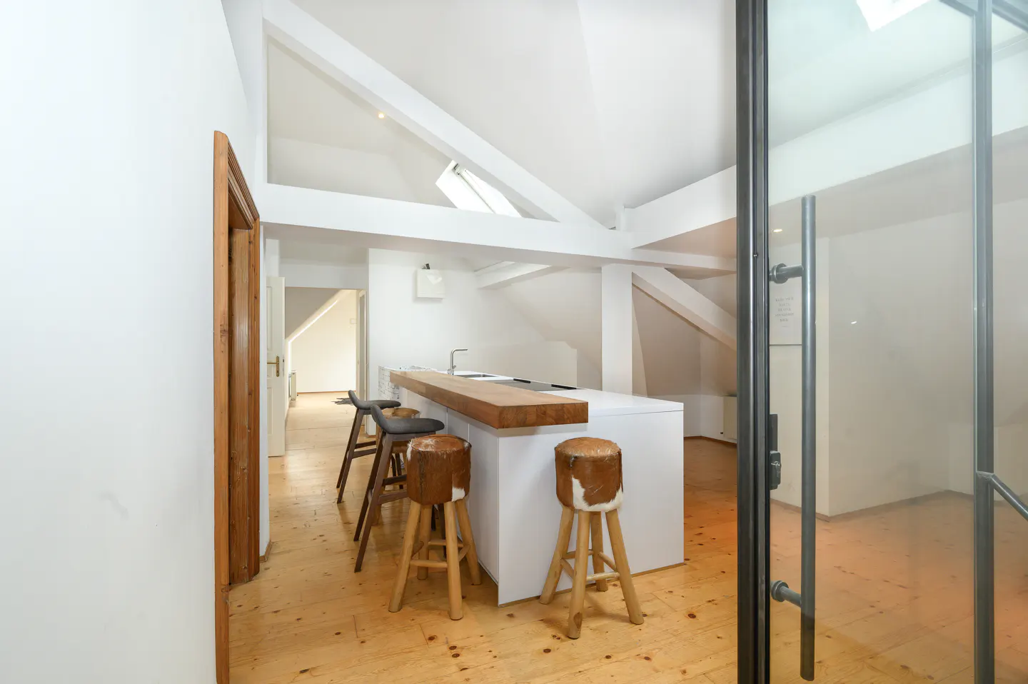 Bright, modern kitchen with white walls, wood floors, and exposed beams. A white island with a wood countertop and stools is featured.