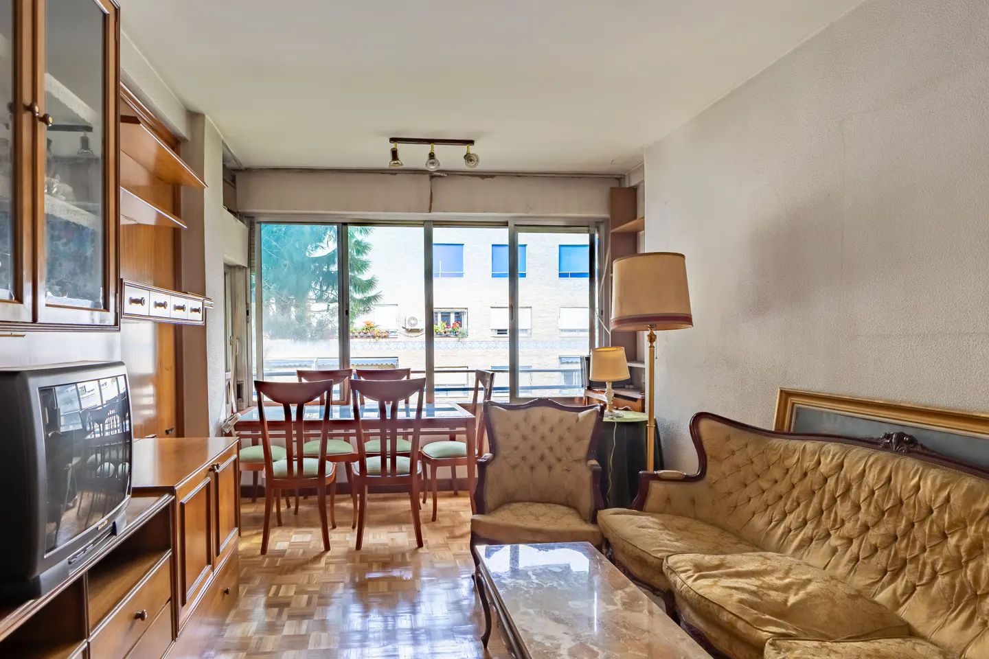 A living room with a dining area, featuring a brown sofa, chairs, and a large window with a view of a building.