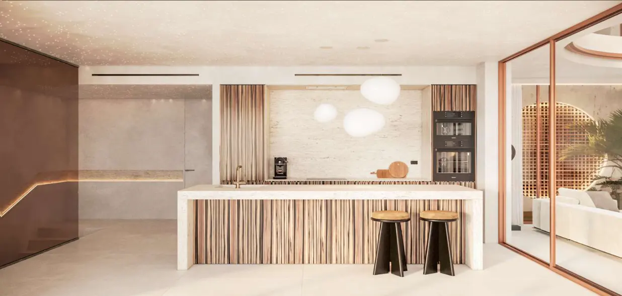 A modern kitchen with a white countertop island, wood paneling, and two black stools. A glass door reveals a living room with a white sofa.