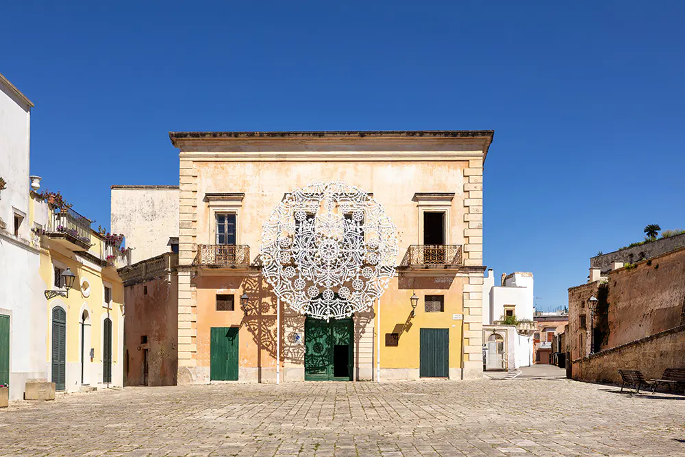 Facade of a yellow building with a large white lace decoration above a green door. Blue sky.