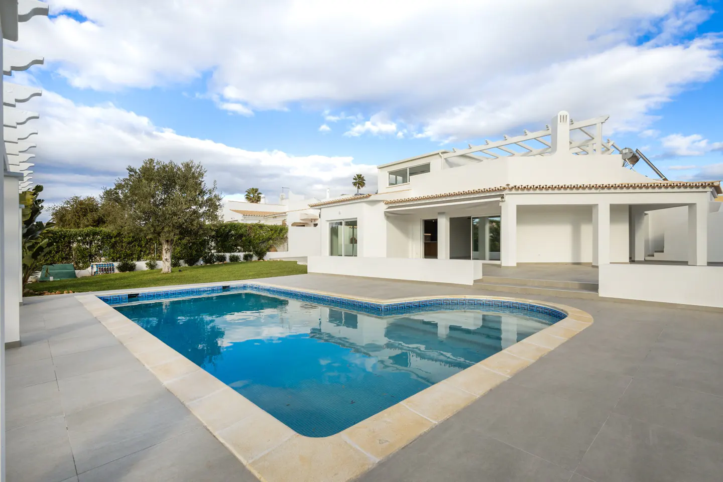 A modern white house with a blue pool and a gray patio under a partly cloudy sky.