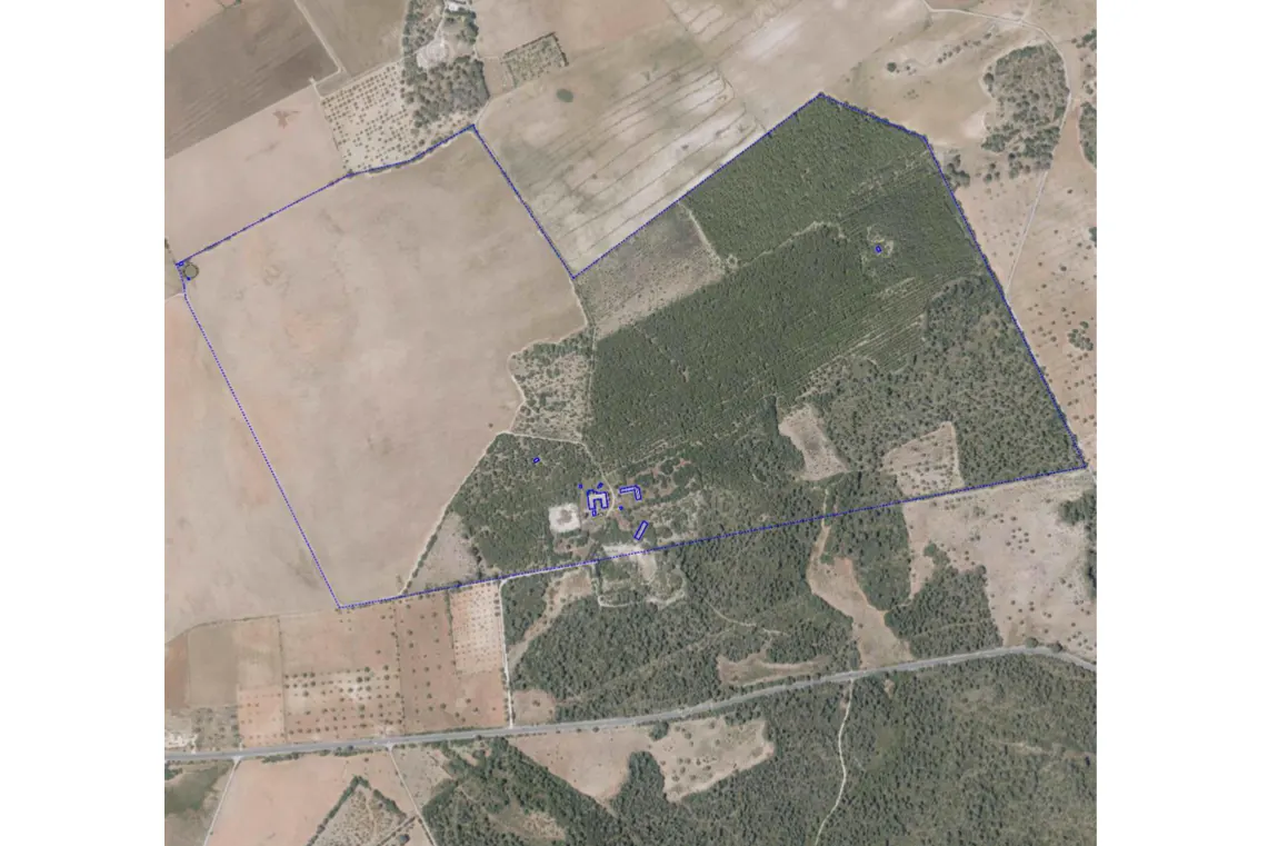 Aerial view of a large property outlined in blue, featuring fields, trees, and a building complex.
