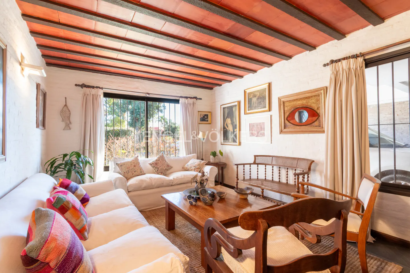 Living room with white sofa, colorful pillows, wooden coffee table, and exposed terracotta ceiling beams.