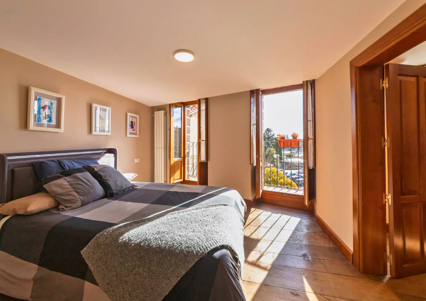 Bedroom with a gray and black checkered comforter, wood floors, and open balcony doors.