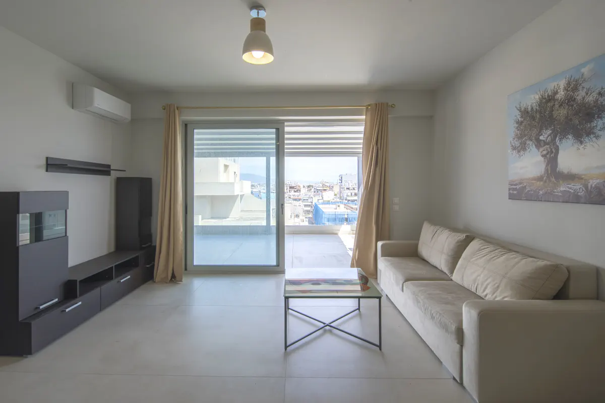 Bright living room with a beige sofa, black media center, and a sliding glass door to a balcony with a city view.