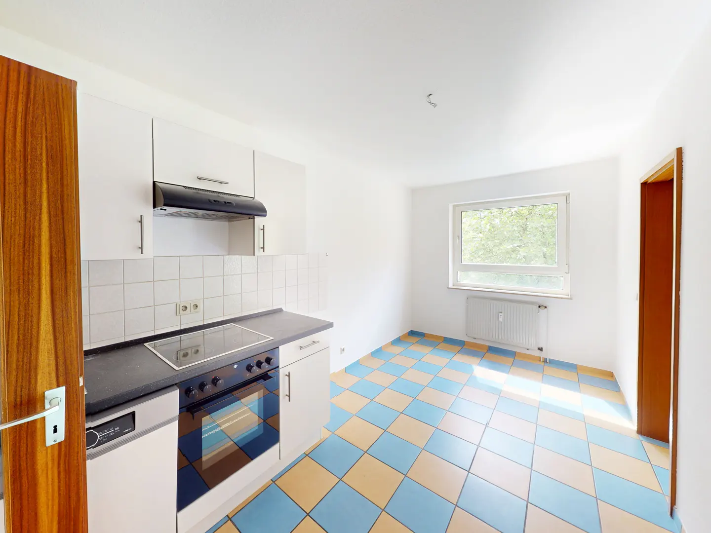 Bright kitchen with white cabinets, black countertops, a stove, and a blue and beige checkered tile floor.